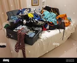A suitcase emptied out onto a bed, its contents spread across the covers