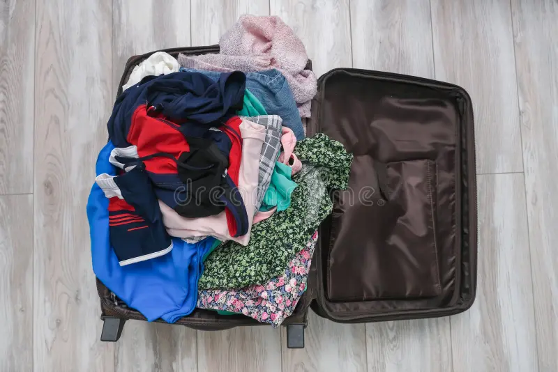 An open suitcase overflowing with a heaped, unsorted pile of clothes